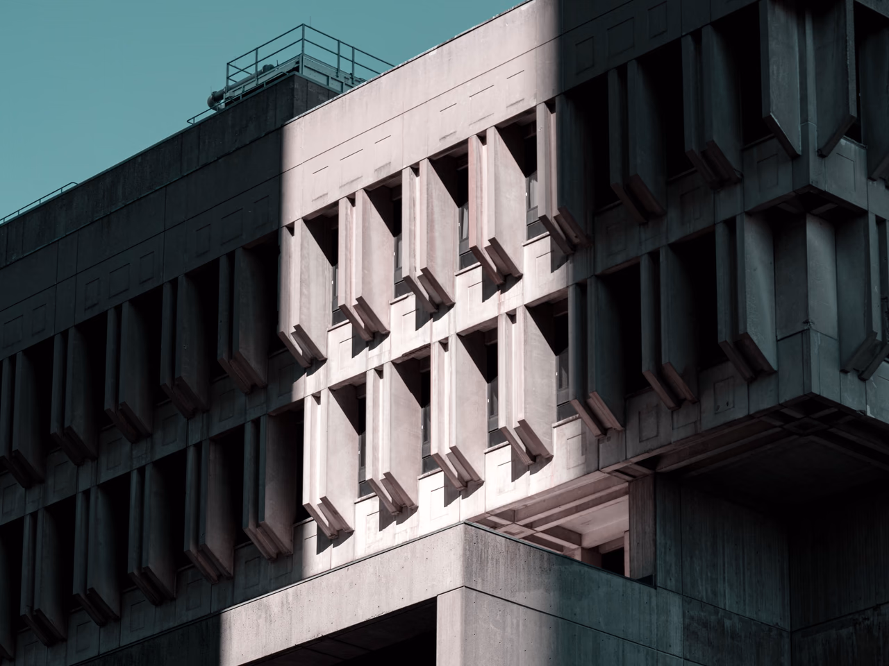 A concrete building with a geometric shape; sunlight casts a sharp shadow on the wall.