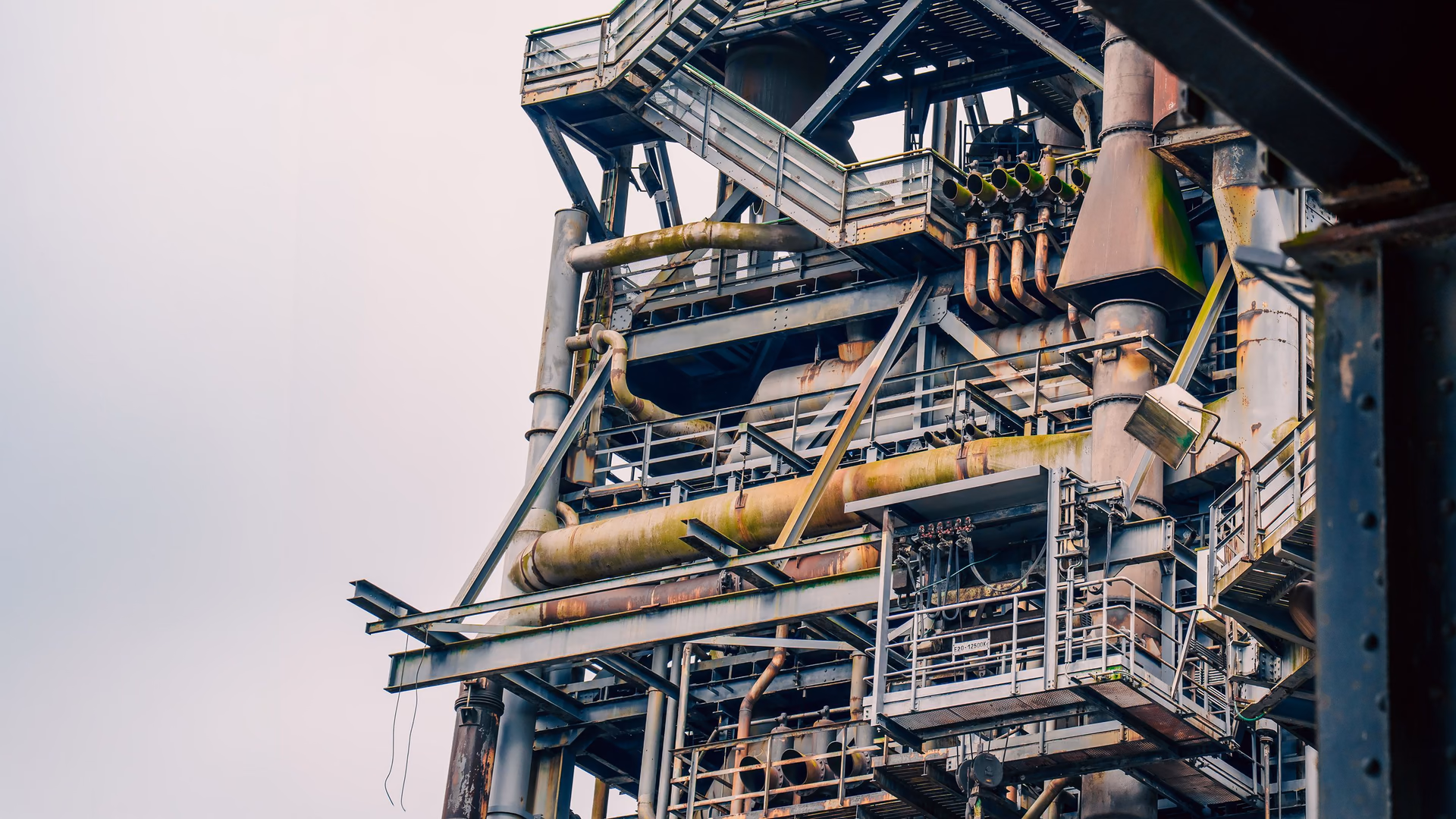 A tower of an industrial plant with pipes, stairs and platforms, seen from the side.